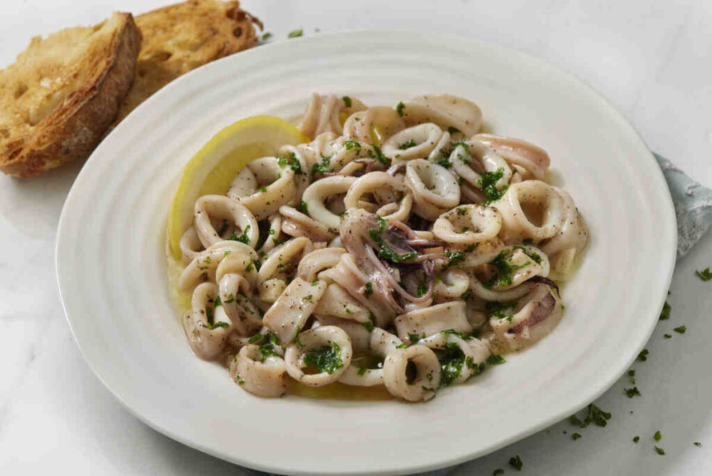 Piatto di calamari grigliati con sugo di limone e prezzemolo in piatto