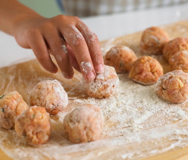 Woman rolling minced meatballs into flour