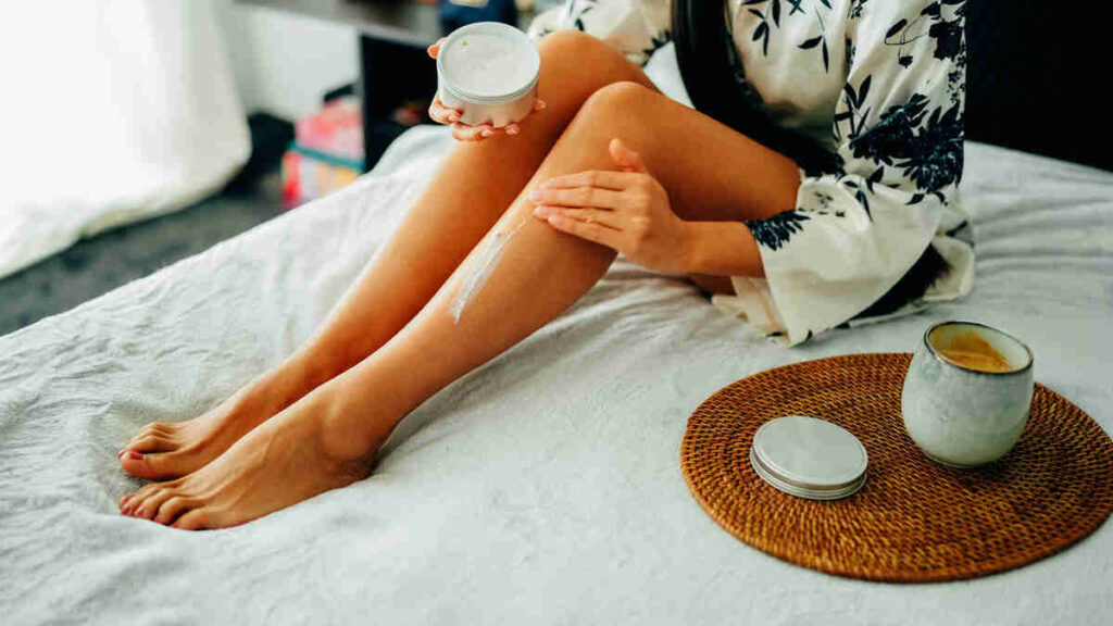 corpo di donna che mette crema su gambe