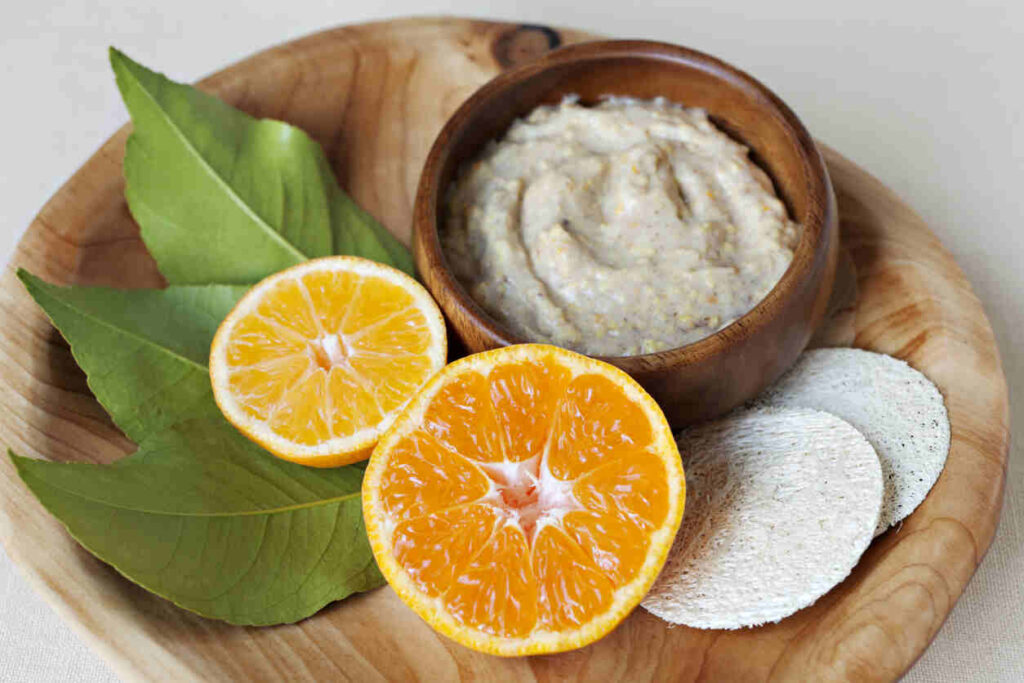 ciotola con preparato maschera viso fai da te, arance, foglie alloro e batuffoli