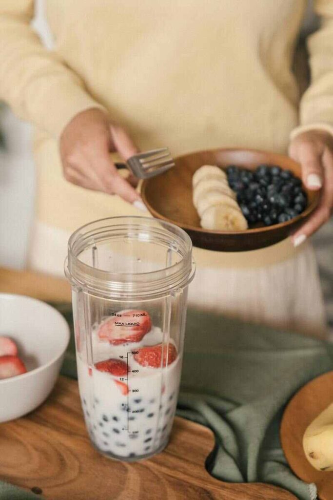 Donna con in mano piatto di frutta (banane e mirtilli) da versare in frullatore con latte e fragola