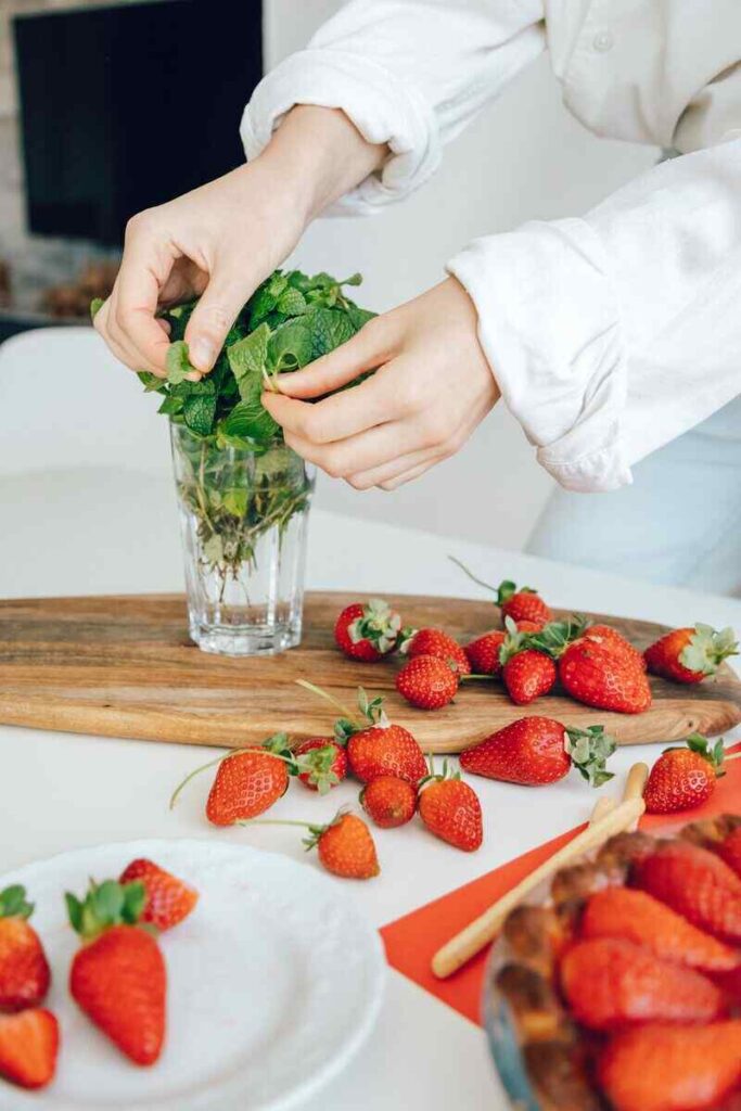 Tavola con fragole e mani di donna con vaso con menta