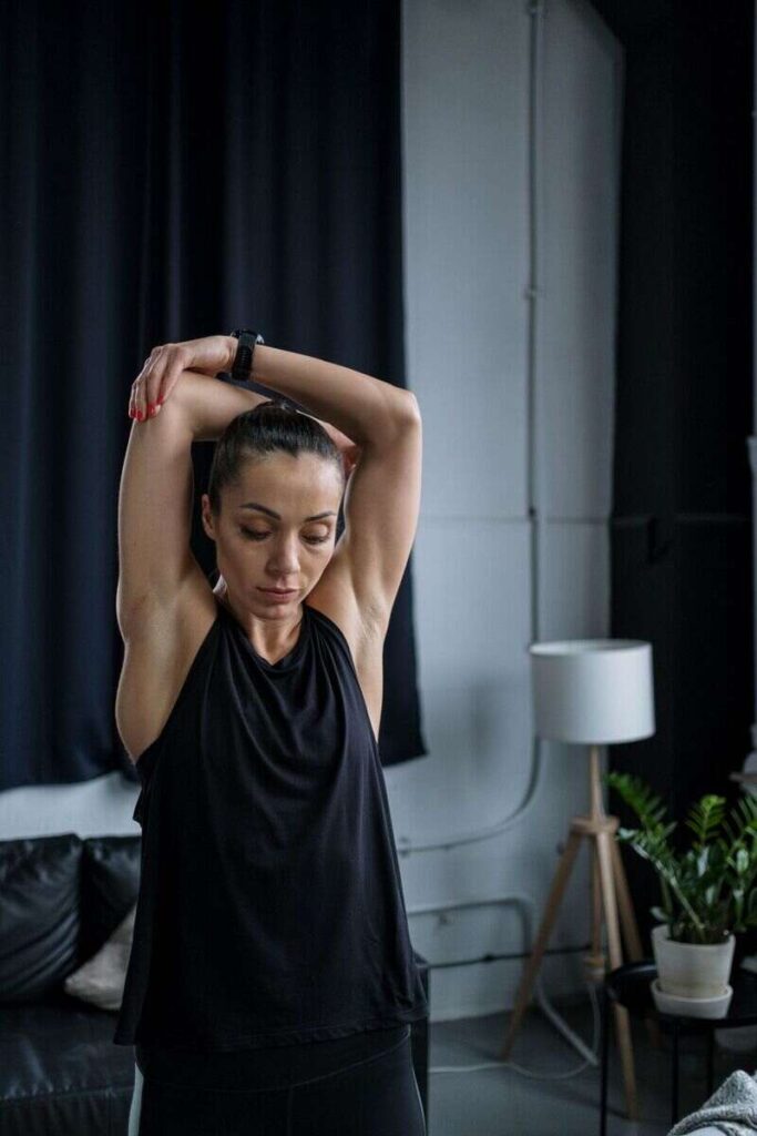 Donna che fa esercizi di stretching con braccia sollevate e mano che tocca gomito e allunga