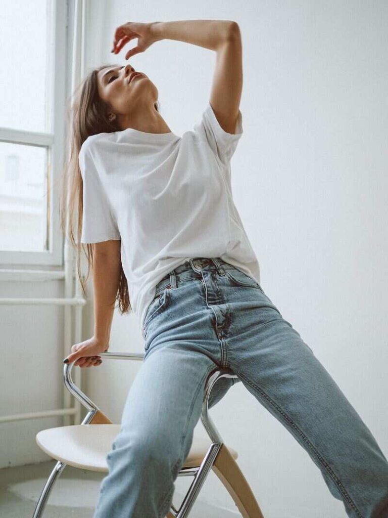 ragazza che indossa t shirt bianca e jeans appoggiata su sedia con testa all'indietro