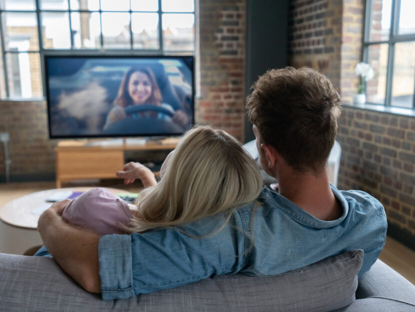 Una coppia abbracciata sul divano guarda la televisione
