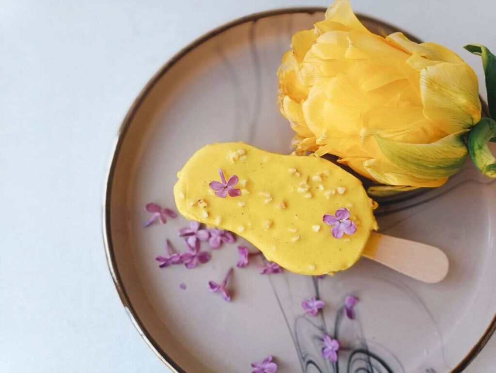 Gelato giallo con fiorellini lilla e fiore giallo a lato su piatto