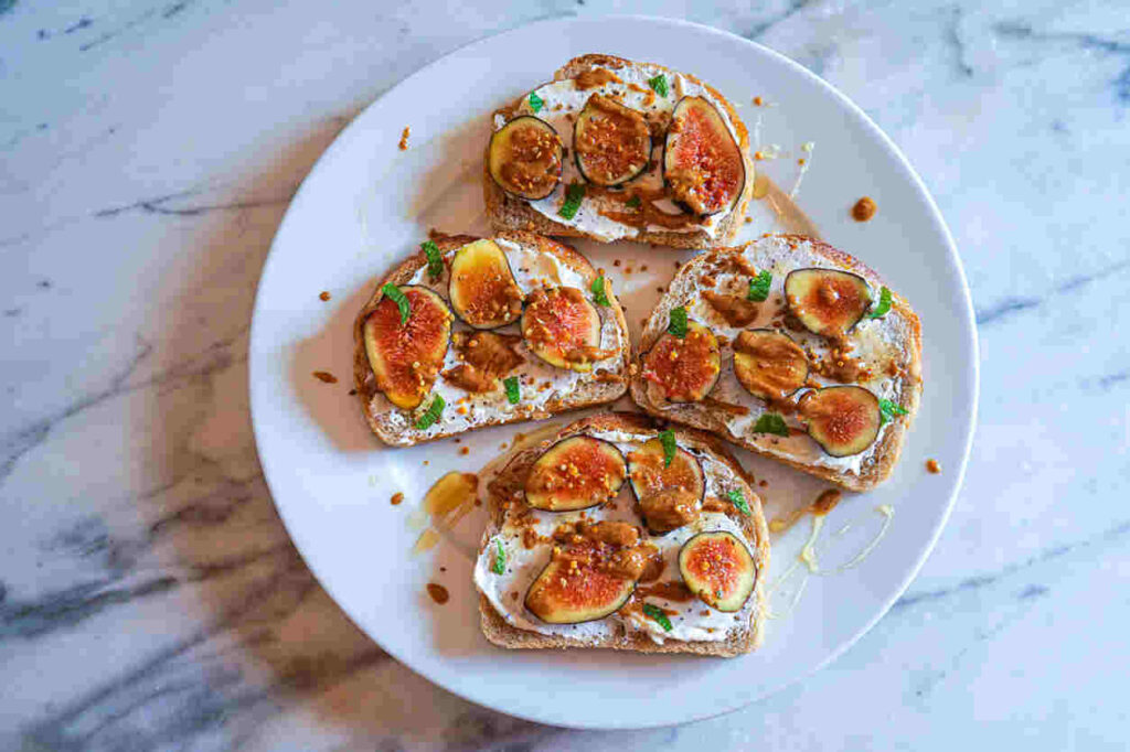 quattro bruschette con fichi e ricotta su piatto bianco