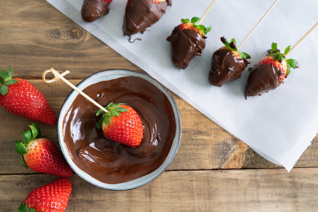Fragole ricoperte di cioccolato su carta da forno e ciotola di cioccolato