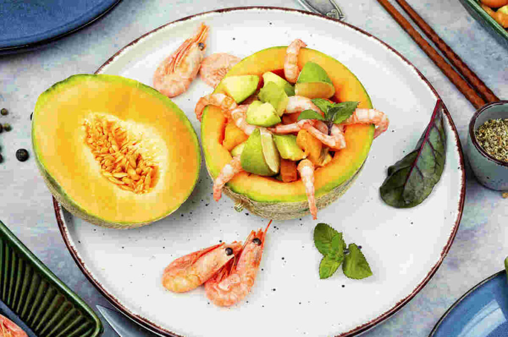 melone tagliato a metà ripieno di gamberi e lime in piatto