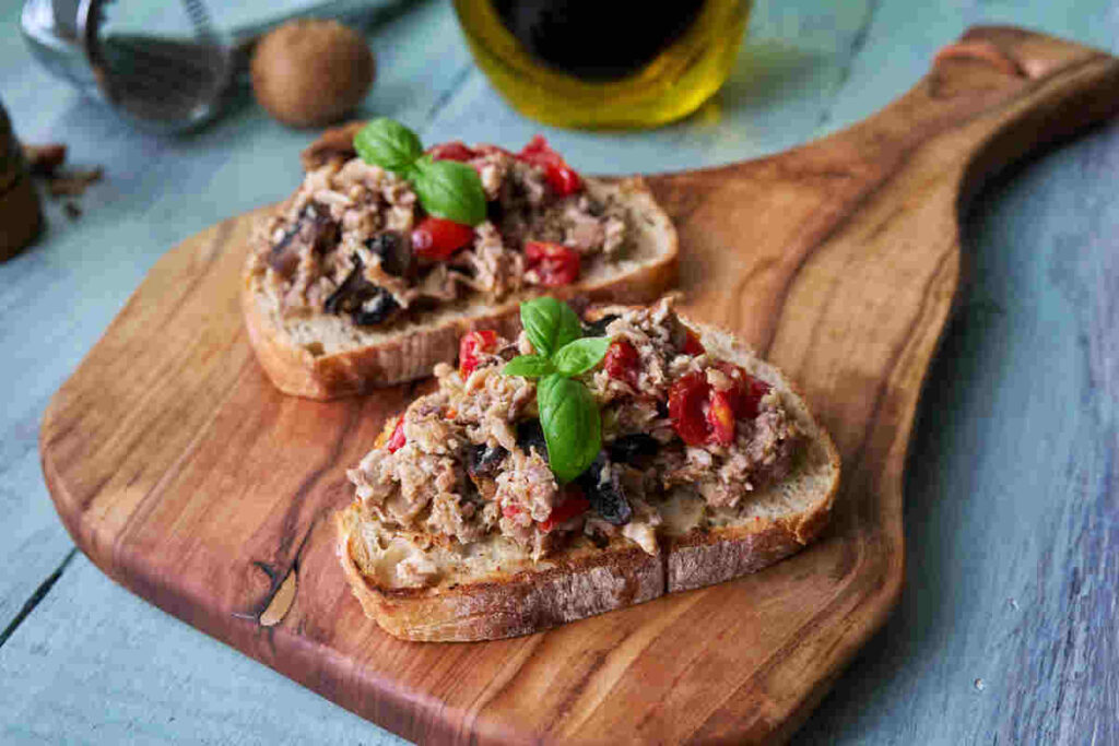 Tonno e pomodorini su fette di pane su tagliere di legno