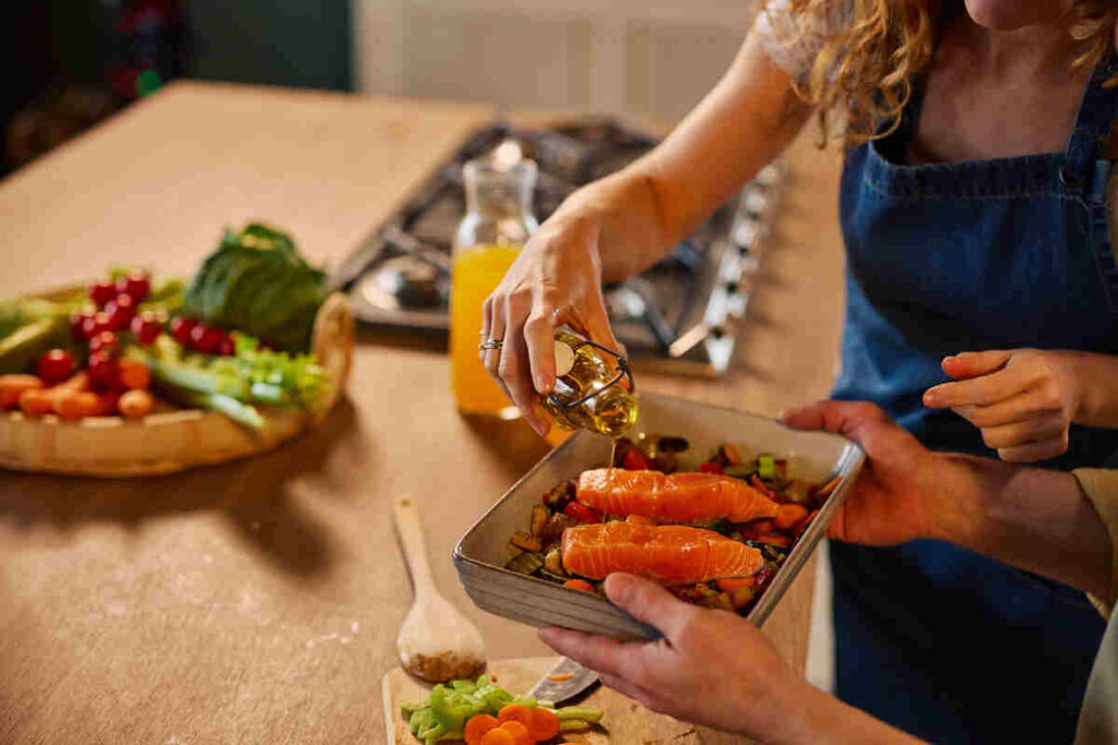 Mani di donna che condiscono salmone con olio 