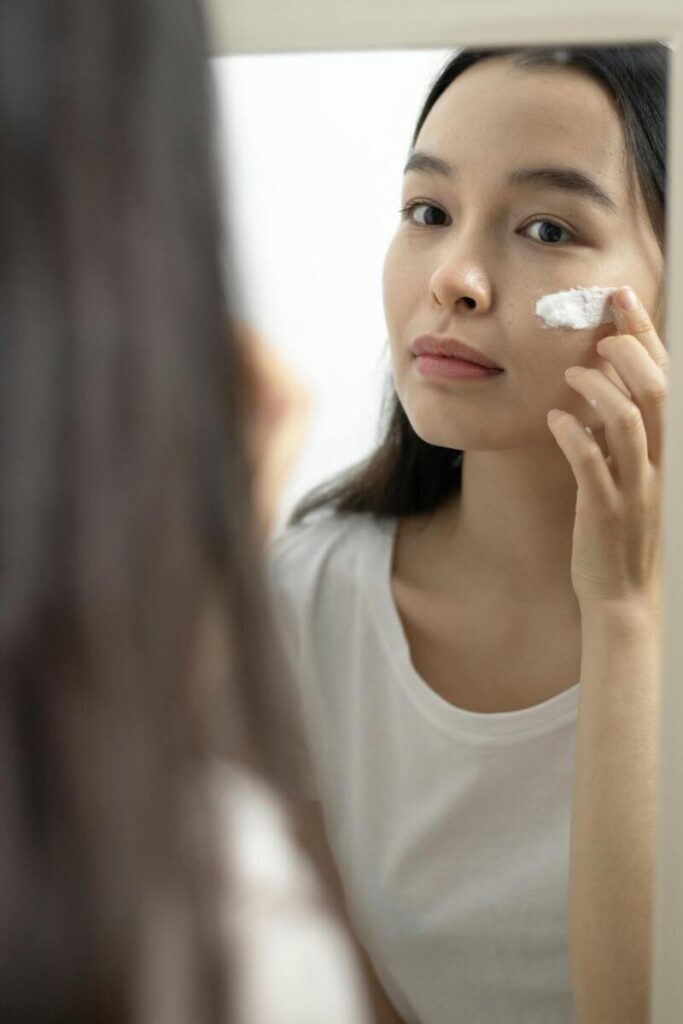 Ragazza asiatica che applica crema sul viso davanti lo specchio