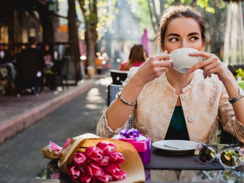 donna beve un caffè al bar, fiori sul tavolo