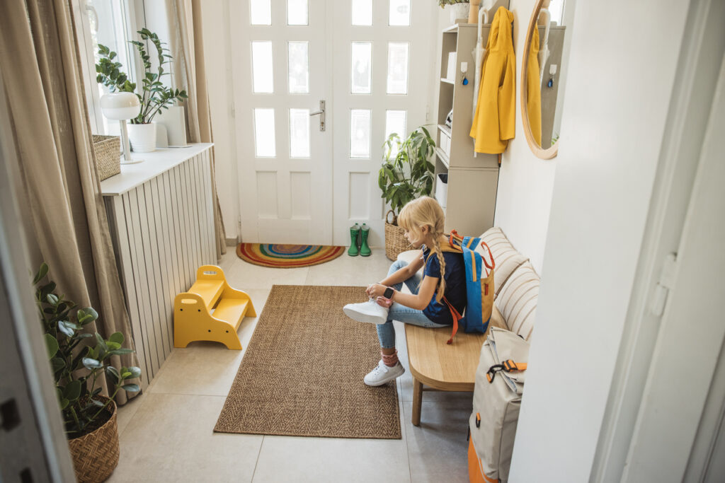 bambina si mette le scarpe seduta su una panca all'ingresso