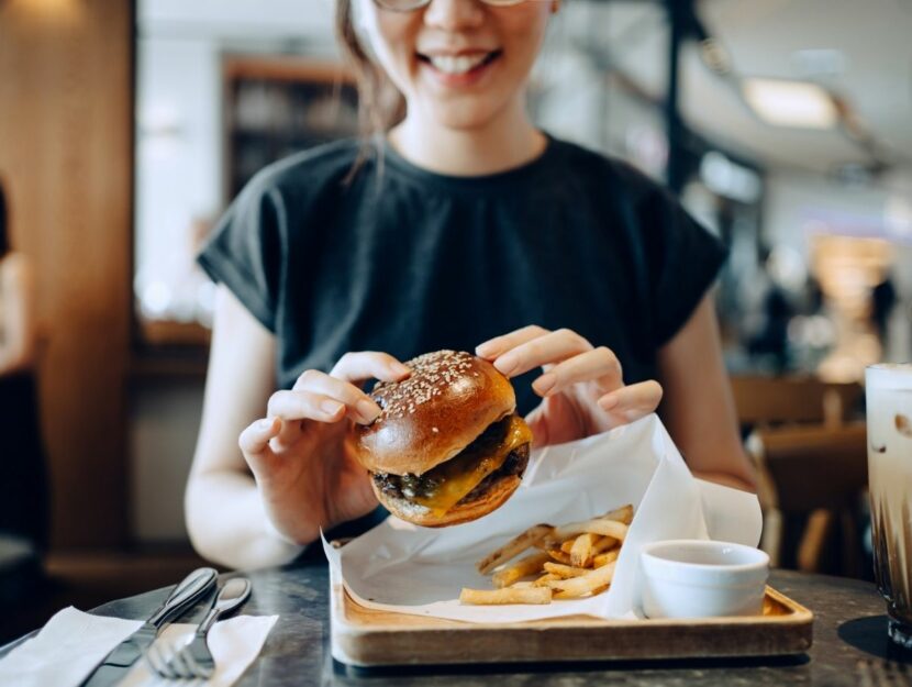 donna che mangia hamburger, cattive abitudini, fast food