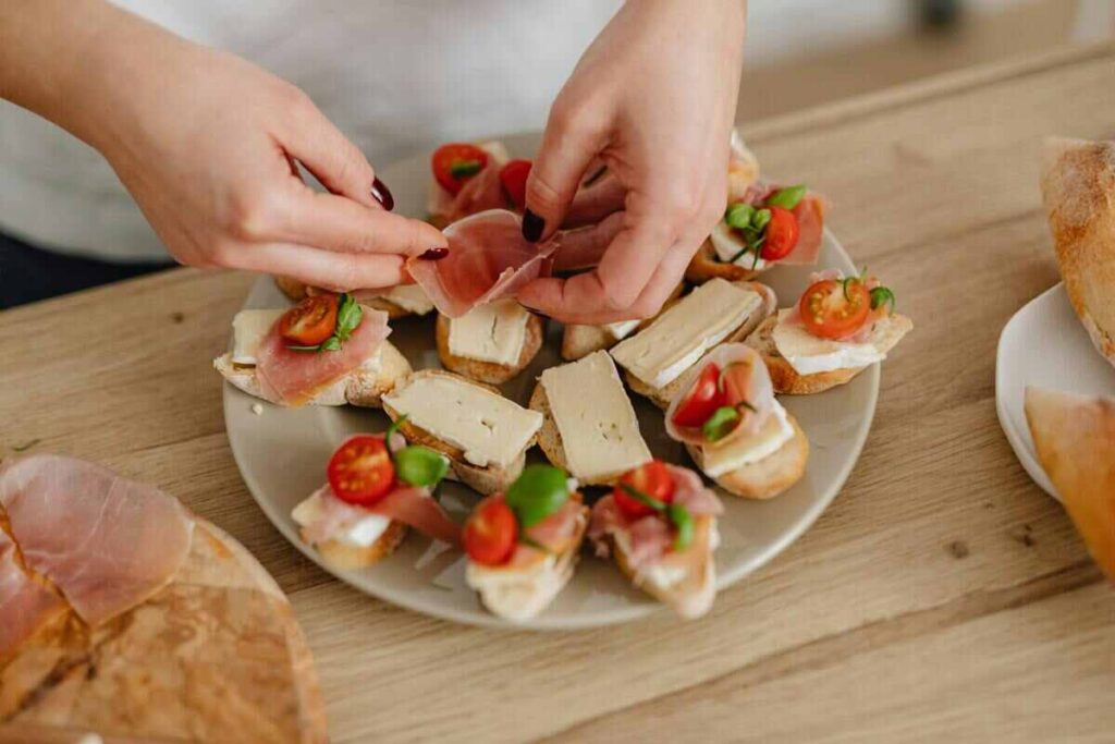 Mani di donna che prepara bruschette con prosciutto in piatto  