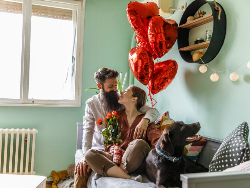 Una coppia di innamorati seduti sul divano con il loro cane festeggiano san valentino