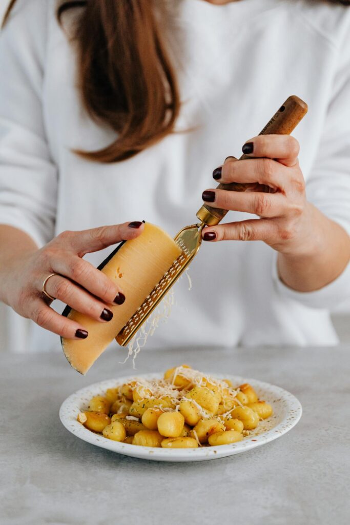 donna sta grattugiando il parmigiano su un piatto di gnocchi di zucca