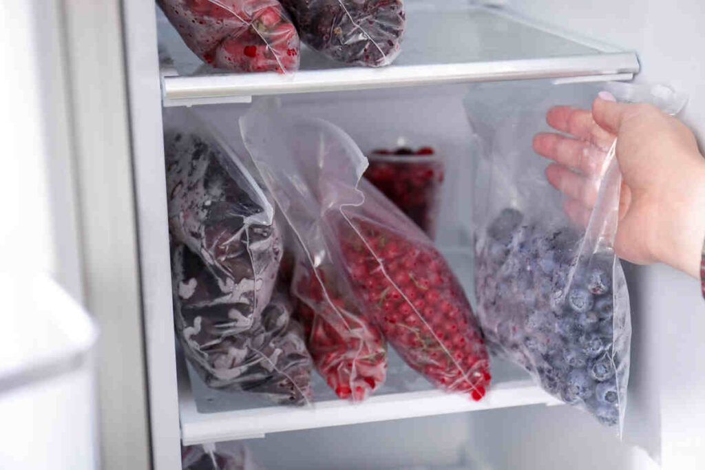mani di donna che mettono sacchetti di frutti rossi nel freezer