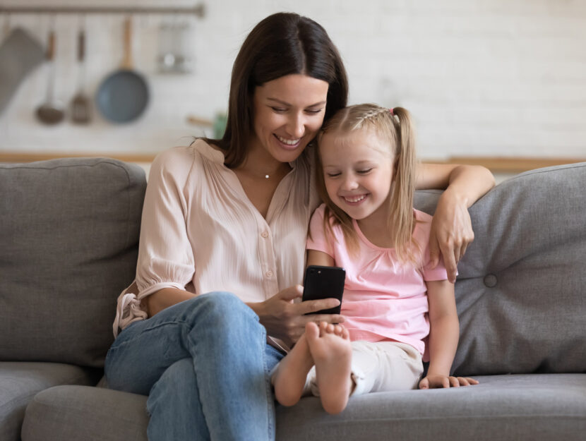donna sorride con la figlia usando lo smartphone
