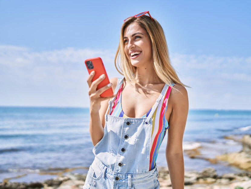 Donna con smartphone sorride in spiaggia