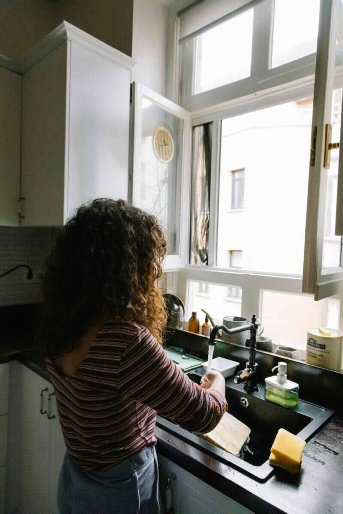 Donna si spalle che lava piatti in cucina con finestra aperta