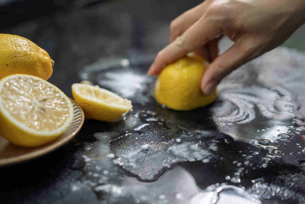 mano di donna che pulisce piano di lavoro con limone e acqua