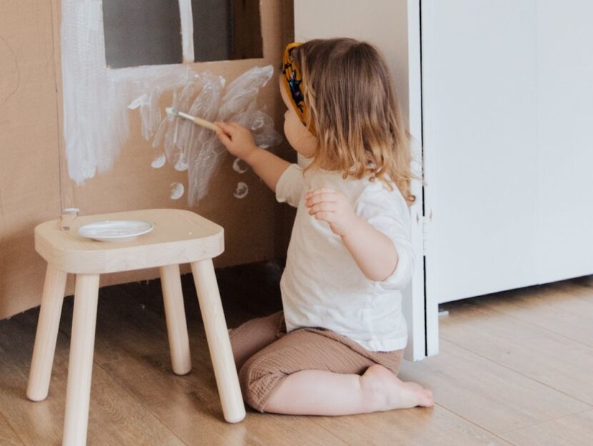 Una bambina sta dipingendo un vecchio scatolone adibito a casetta