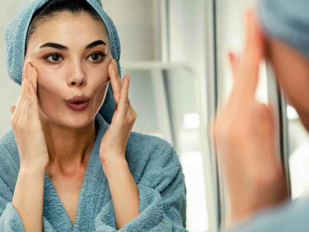 Una donna fa yoga facciale davanti allo specchio