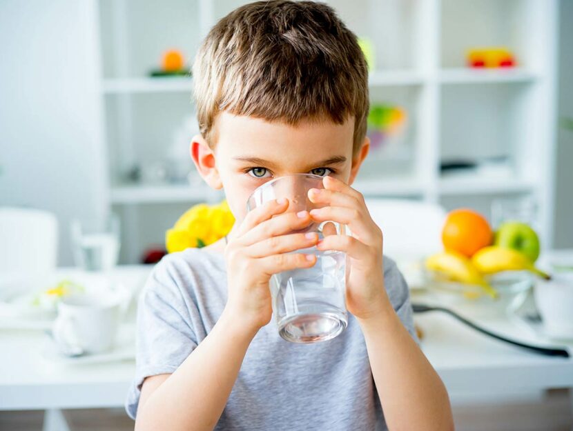 Bambino beve acqua da un bicchiere in cucina