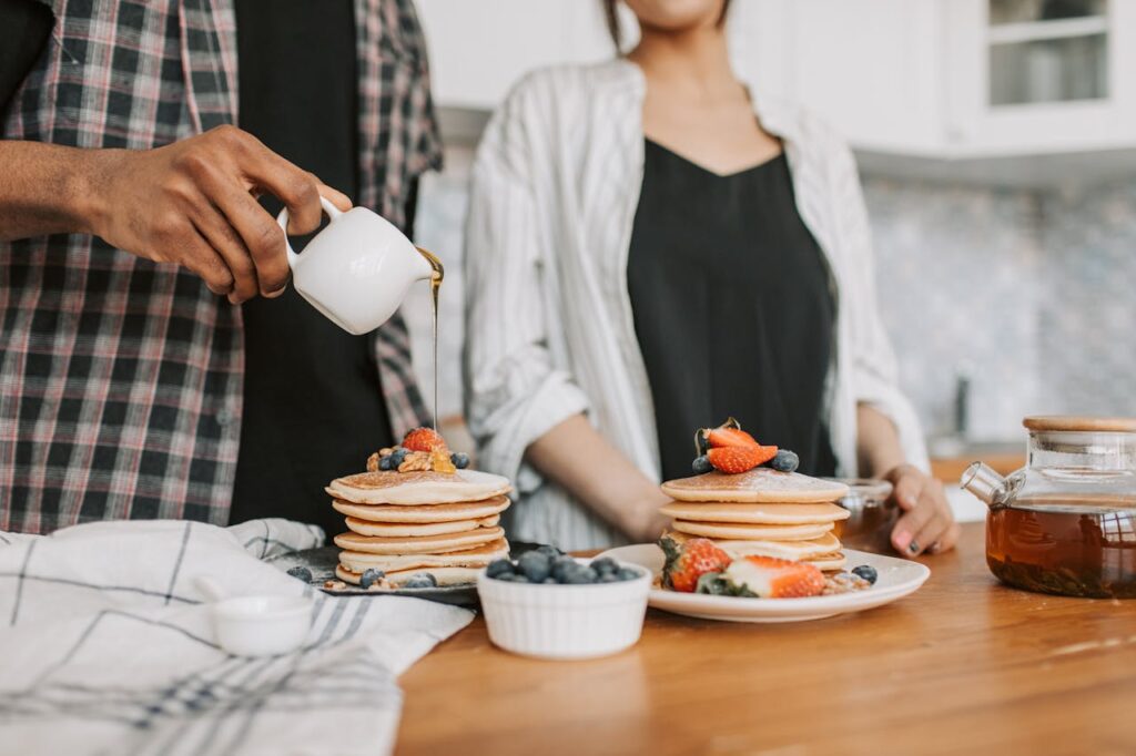 due persone versano lo sciroppo d'acero sui pancakes