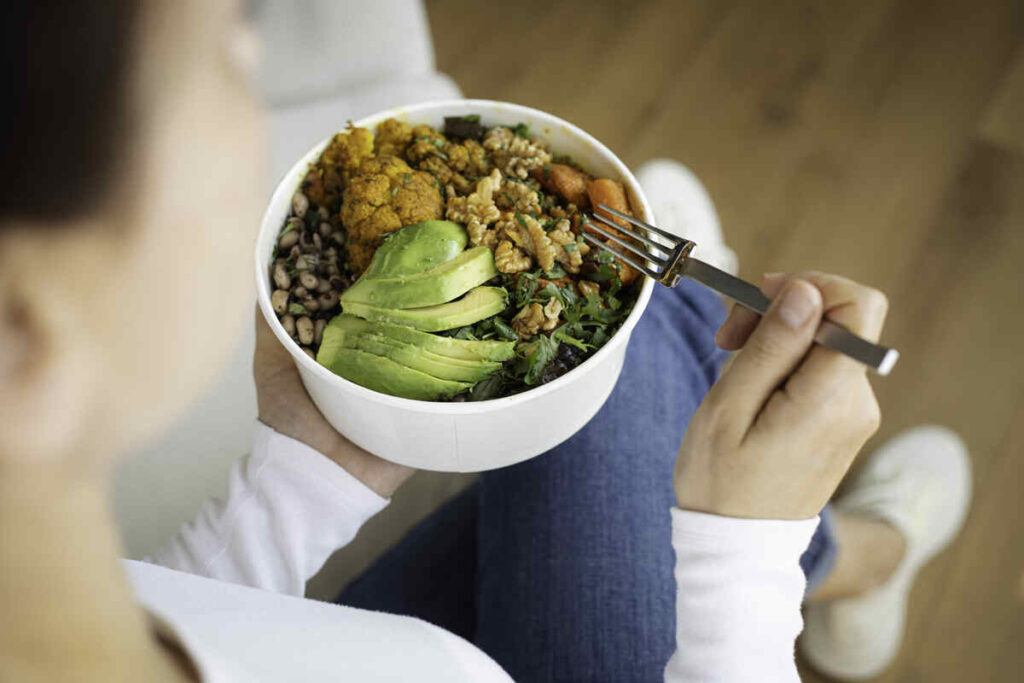 donna che mangia bowl con avocado, verdura, cereali