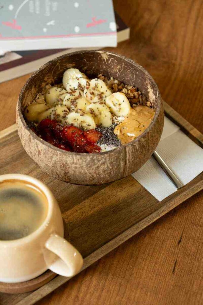 Ciotola a forma di cocco con porridge di banana, semi di chia e burro d'arachidi con tazza di caffè vicino