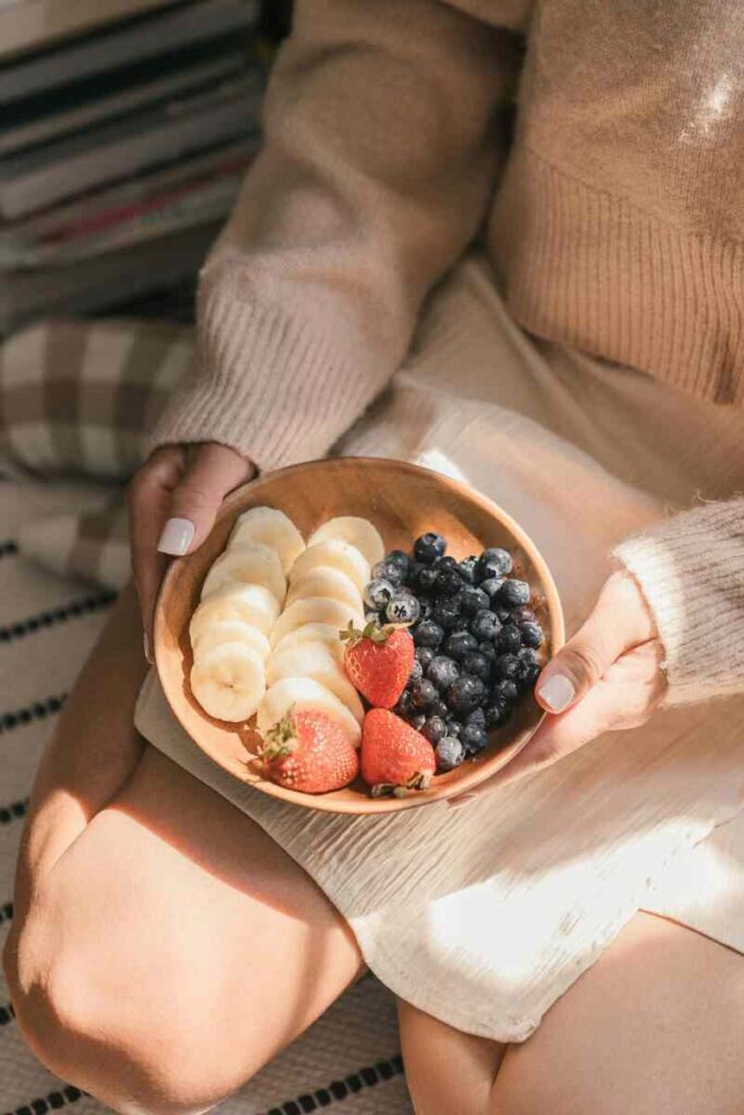 Donna che ha in mano una ciotola di frutta con banana, fragola e mirtilli