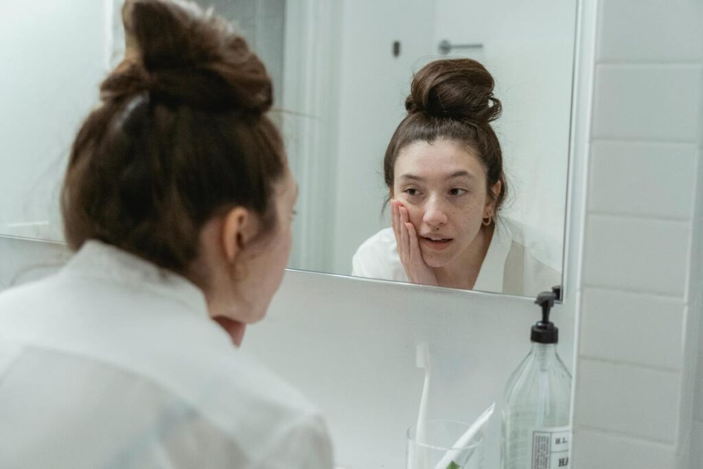 Ragazza con capelli raccolti e accappatoio che si specchia e si applica crema viso