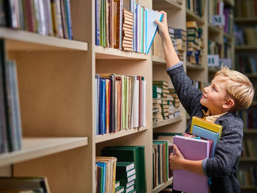 Bambino prende libri da uno scaffale