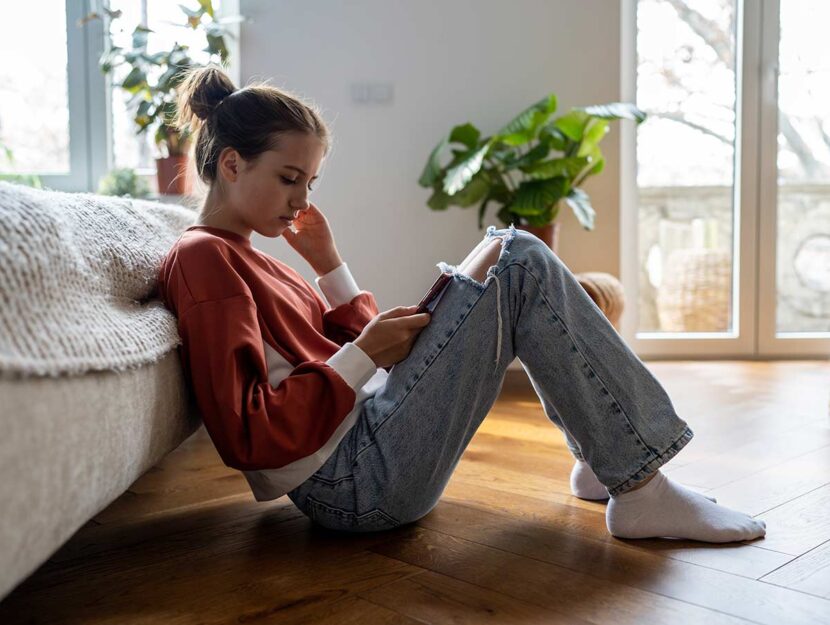 Cyberbullismo, adolescente guarda pensierosa il suo smartphone