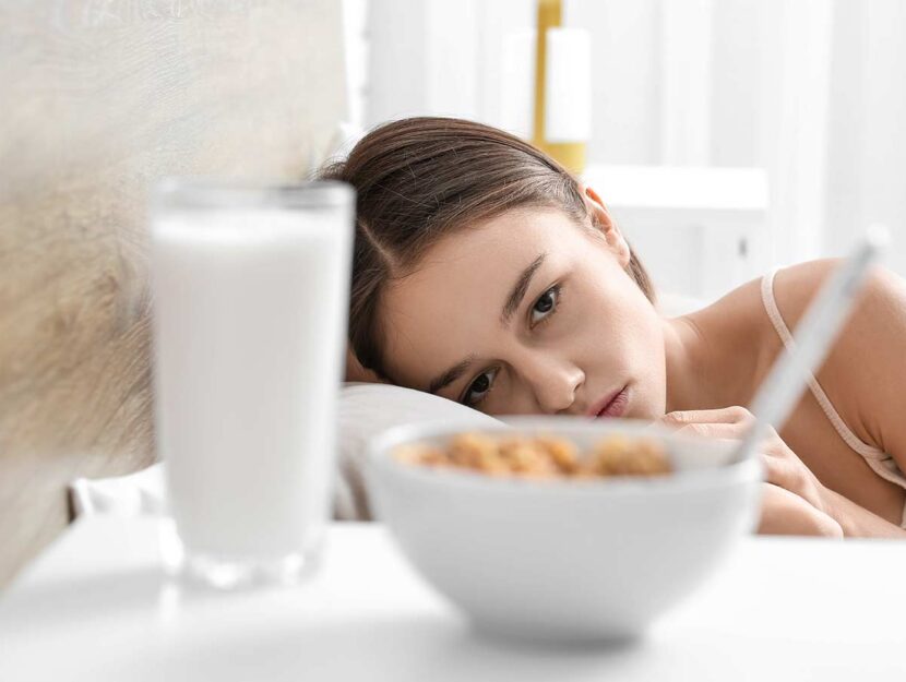 Disturbi alimentari, giovane donna con bicchiere di latte e corn-flakes