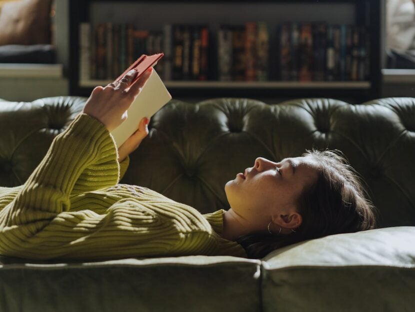 una ragazza distesa sul divano sta leggendo un libro