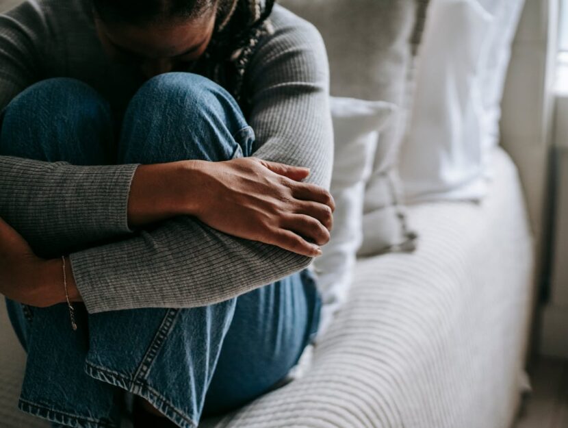 ragazza accoccolata sul letto che si abbraccia le gambe