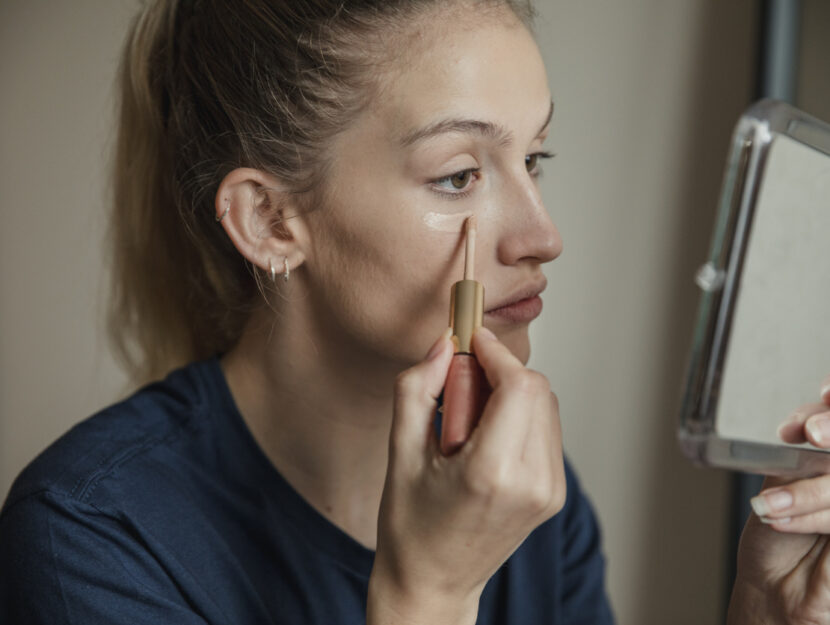 ragazza si mette il correttore sulle occhiaia allo specchio