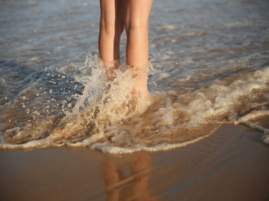 Gambe femminili con capillari nell'acqua del mare in estate