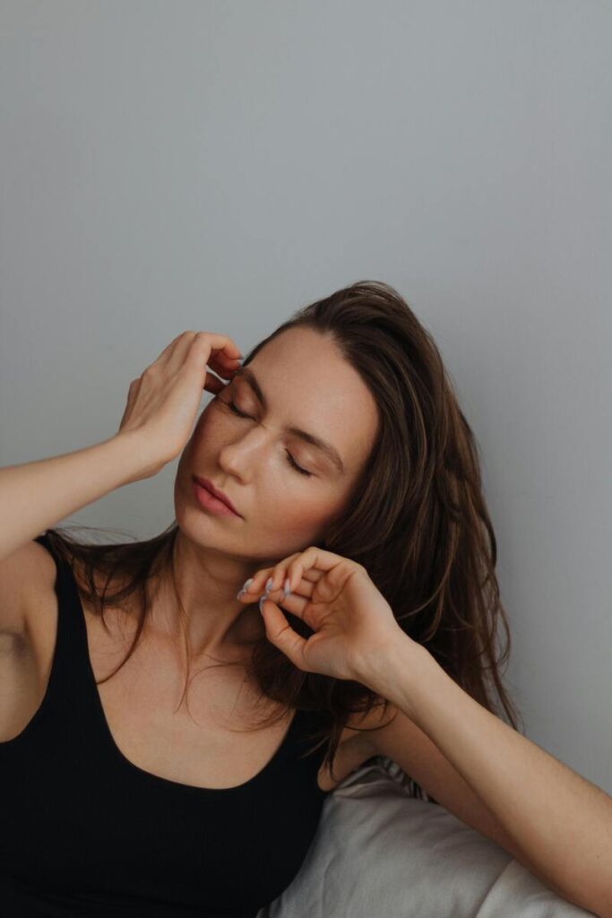 Donna mezzo busto in movimento con capelli lunghi, occhi socchiusi e mani sul viso