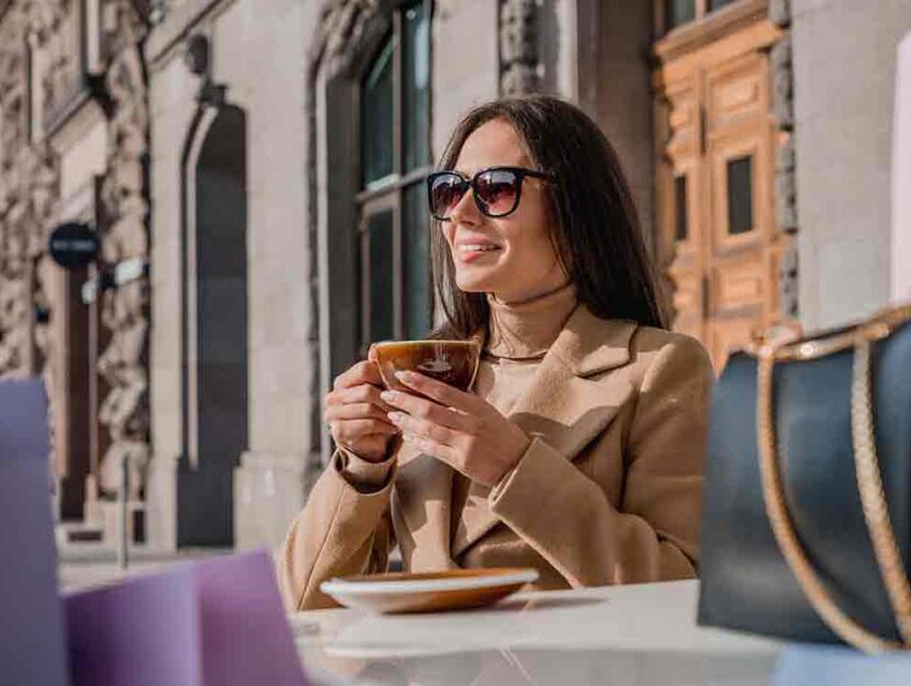 Donna sorridente beve cioccolata al tavolo di un bar all'aperto