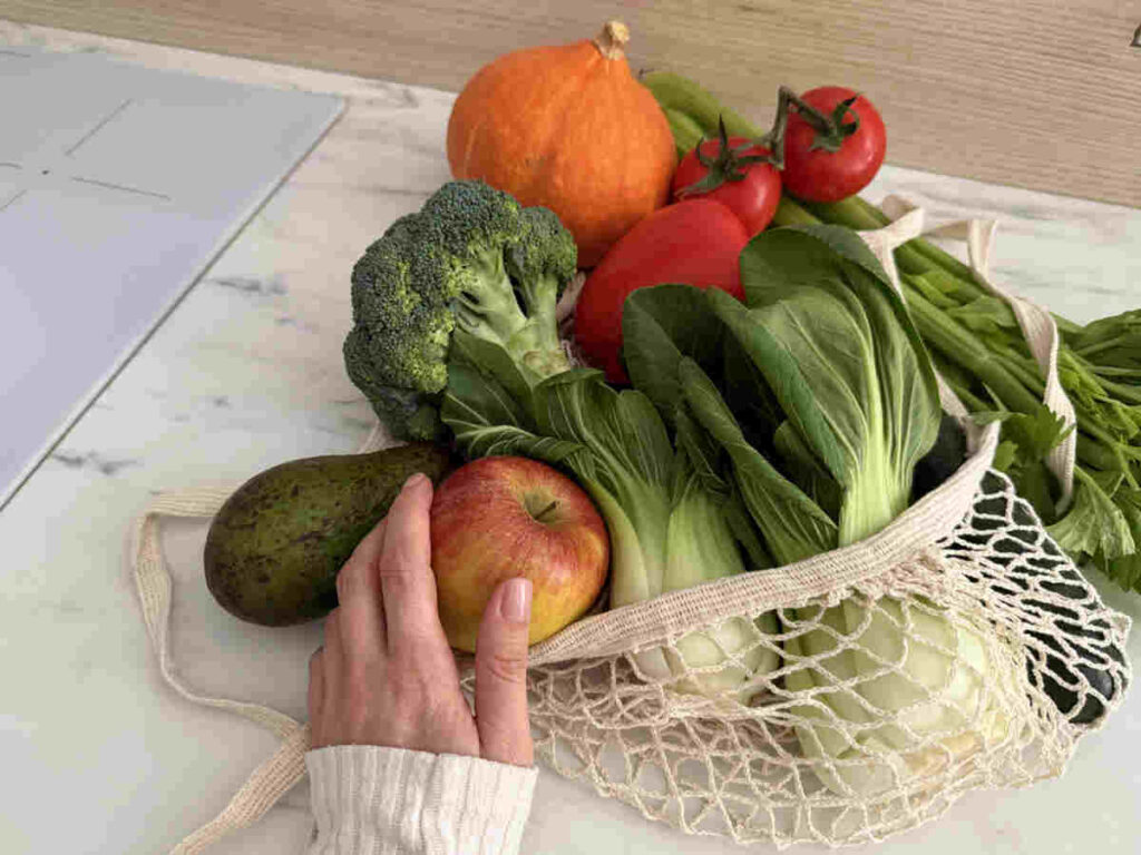 mano di donna con busta con verdure, insalata, mela