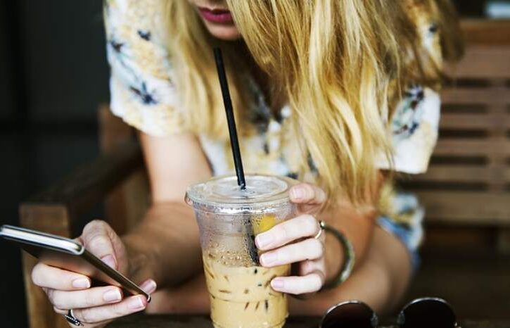 ragazzina allo smartphone mentre beve uno smoothie