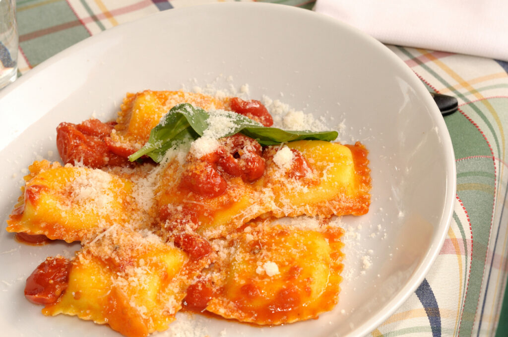 Ravioli al sugo di pomodoro, grana e basilico su piatto bianco