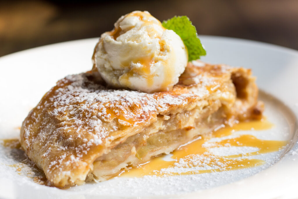 Torta di mele con sopra gelato alla vaniglia e sciroppo su piatto bianco