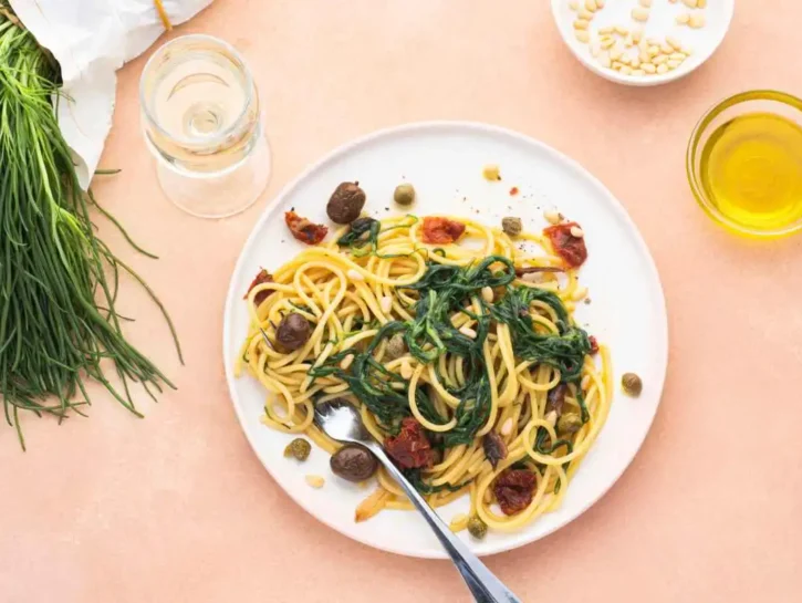 Spaghetti con agretti, olive, acciughe, pomodori, capperi e pinoli
