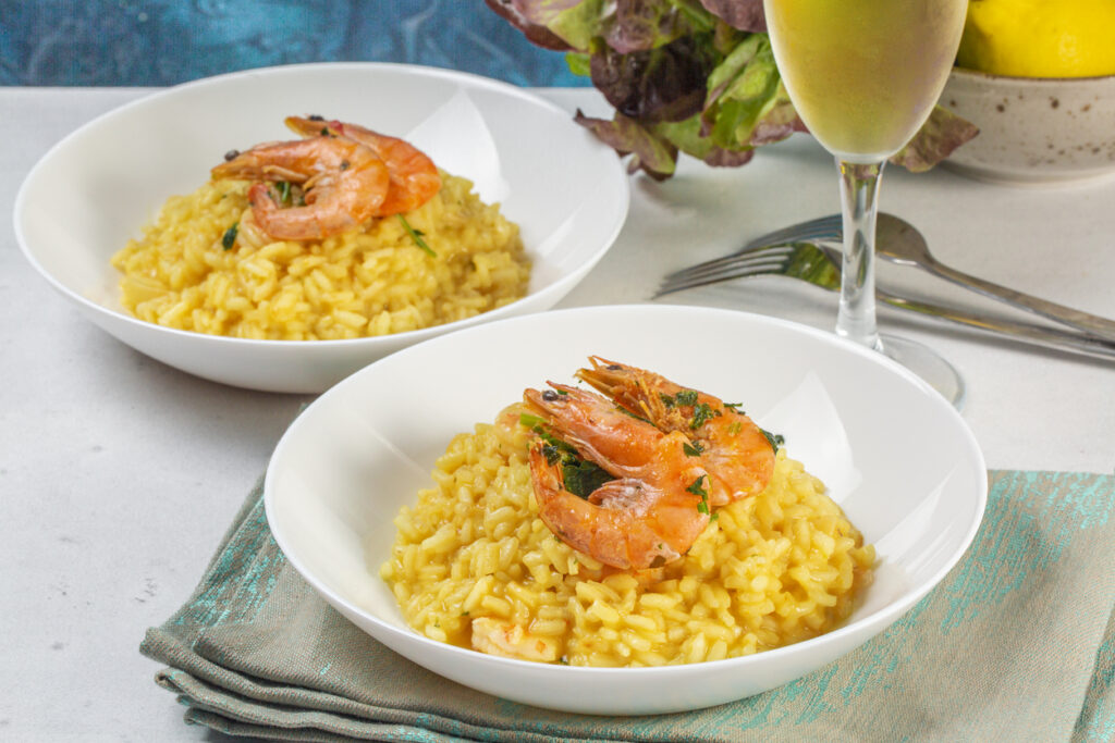 Piatto di riso allo zafferano con scampi accompagnato bicchiere di vino bianco
